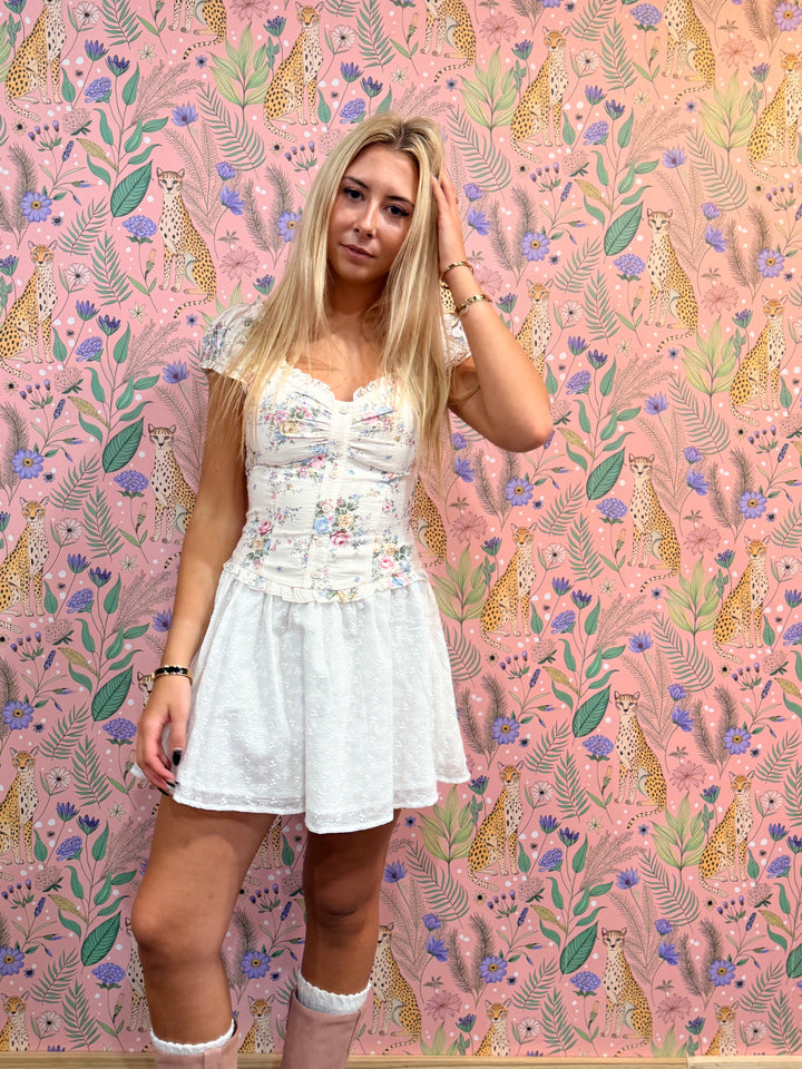 Woman in a white dress standing against a pink floral and animal patterned wall.