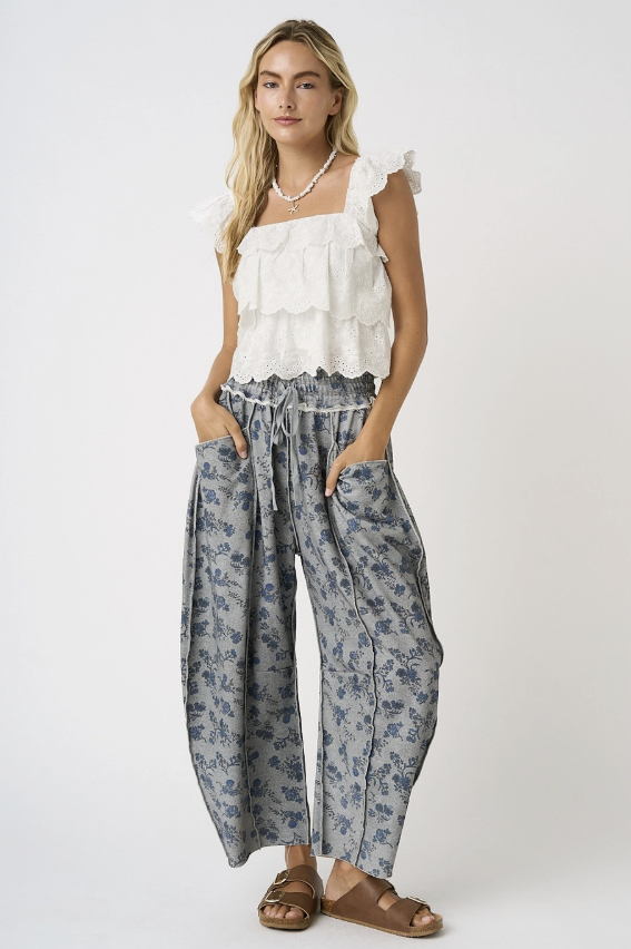 Woman wearing grey floral pants with white flutter top on white background