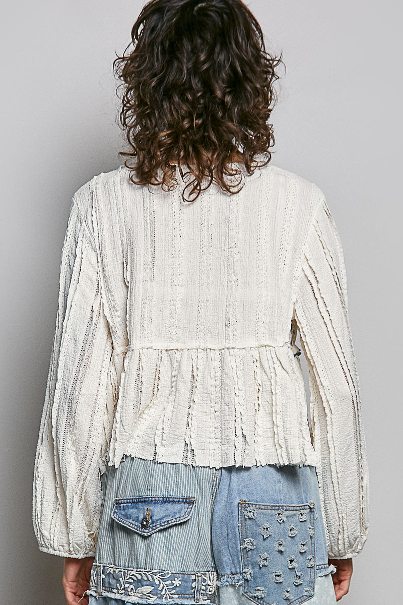 Person wearing a textured white top and denim jeans against a plain background