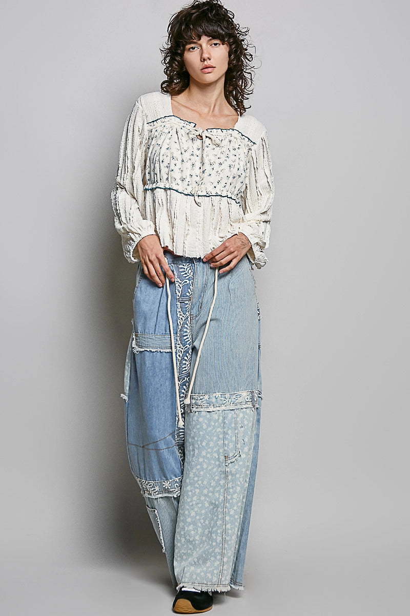 Woman wearing a white blouse with floral patterns and light blue denim pants on a gray background