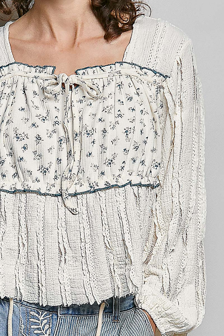 White blouse with floral patterns and blue accents on a gray background