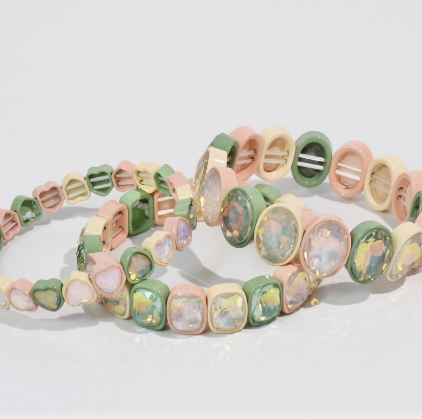 Three pastel-colored stretch bracelets with heart, oval, and square charms, featuring iridescent opal-like resin stones, displayed on a clean white background.