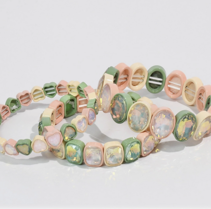 Three pastel-colored stretch bracelets with heart, oval, and square charms, featuring iridescent opal-like resin stones, displayed on a clean white background.