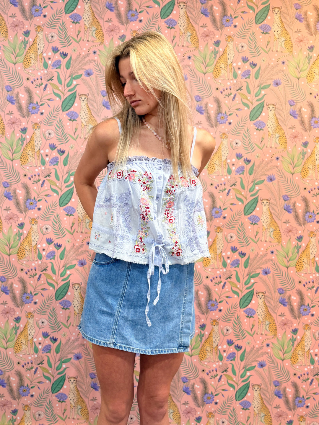 Woman wearing a floral top and denim skirt against a patterned background