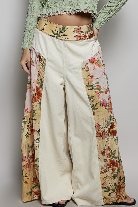 A person wearing wide-leg cream pants with floral printed side panels and a matching floral waistband, paired with a light green cropped top against a plain light gray studio background.