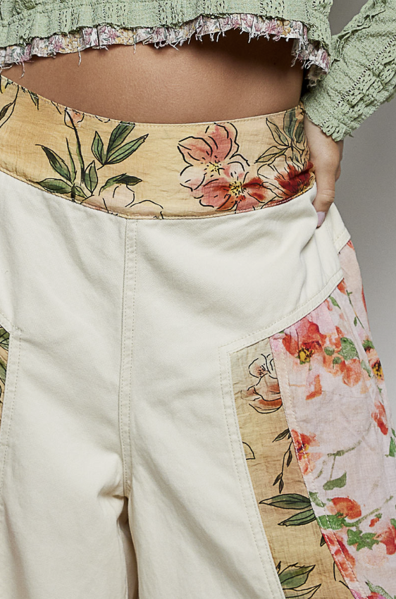 A close-up of a person wearing patchwork wide-leg pants with a cream base and floral printed panels in pink, green, and beige, paired with a green cropped top.