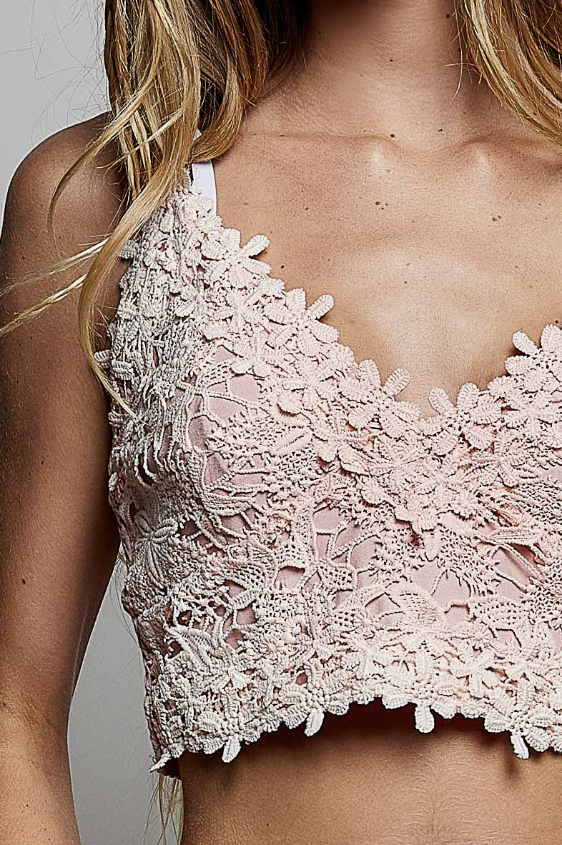 A close-up of a model wearing a pale pink floral lace halter crop top, showing the intricate lace details and scalloped edges.