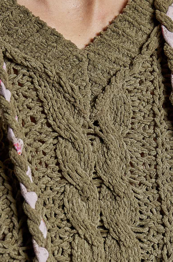 Close-up of a chunky cable-knit sweater in olive green, showing the detailed knit pattern and a V-neckline.