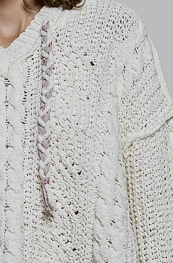 Close-up of a chunky cream cable-knit cardigan sweater with a pink and white braided drawstring, worn by a model.
