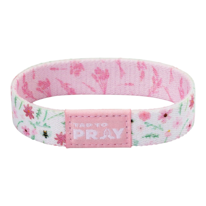 A pink fabric wristband with a floral and bee pattern, featuring a central pink tab that reads &
