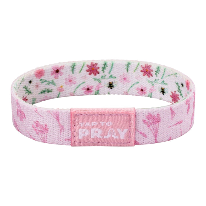 A pink fabric wristband with a floral pattern and a central pink tab that reads &