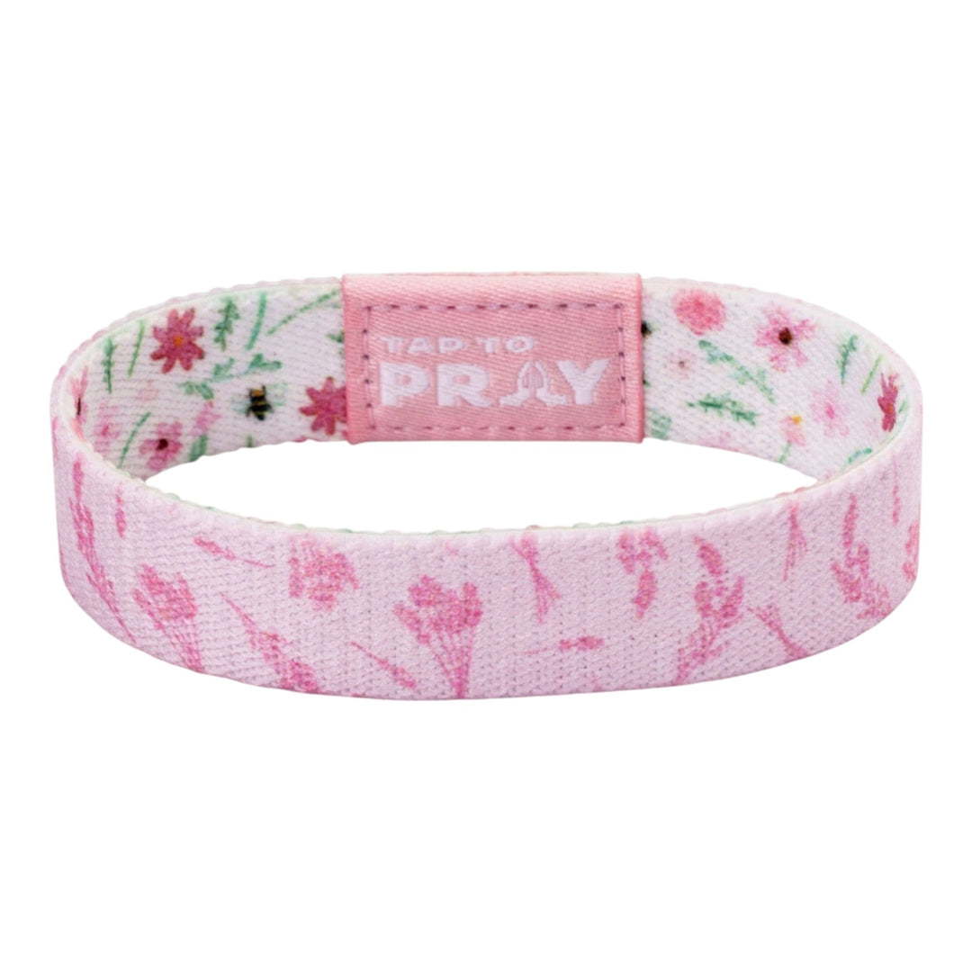 A fabric wristband with a pink and white floral pattern, featuring a central pink tab with the text &