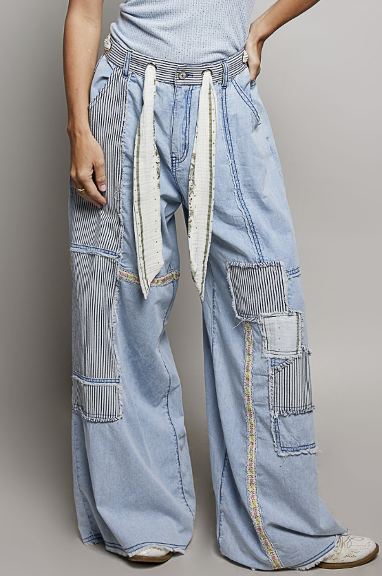 Person wearing light blue patchwork jeans on a plain background