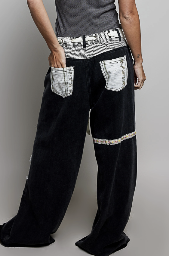 Black wide-leg corduroy pants with distressed white patch pockets and a striped waistband, shown on a model from the back against a neutral gray background.