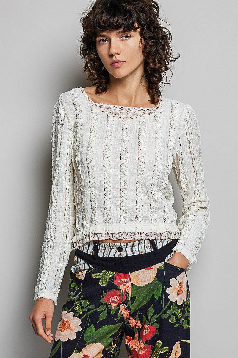 Woman wearing a white lace top and floral pants against a gray background