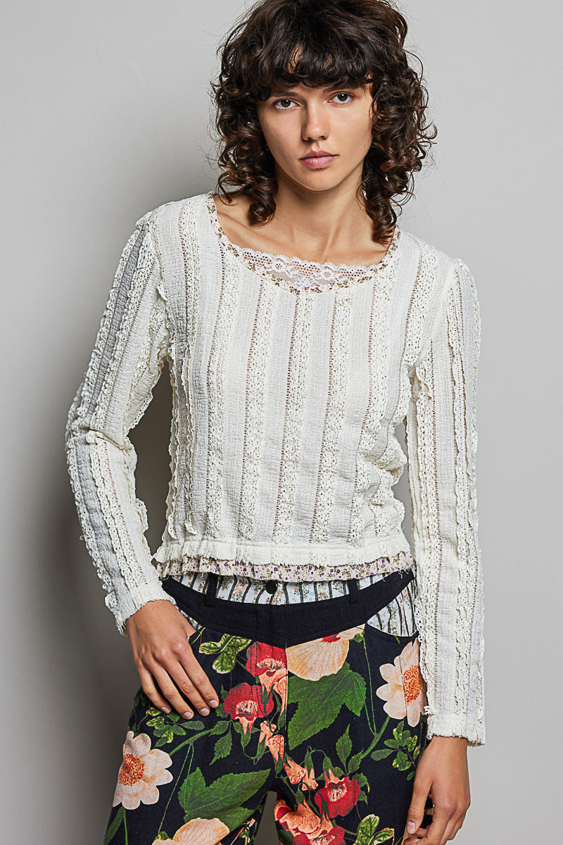 Woman wearing a white lace top and floral skirt against a gray background