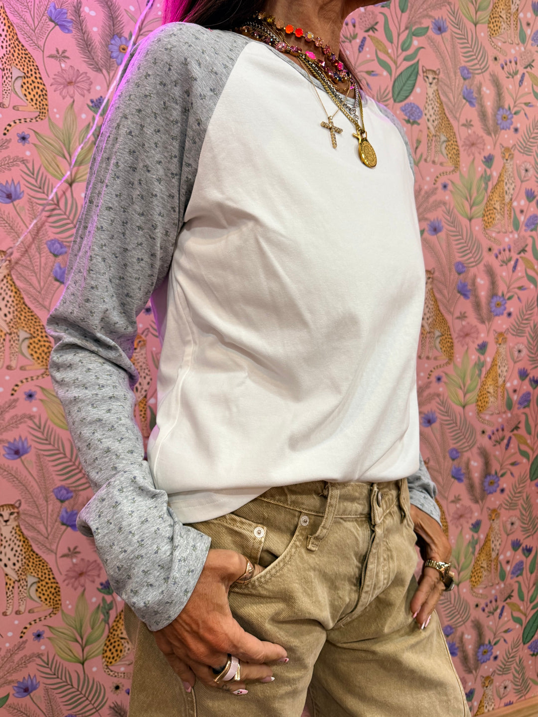 Woman wearing white and grey raglan tee with floral print on sleeves on floral background