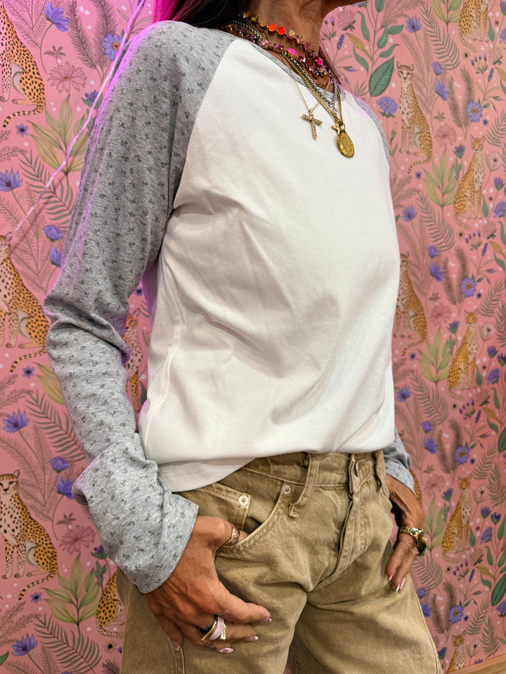 Woman wearing white and grey raglan tee with floral print on sleeves on floral background