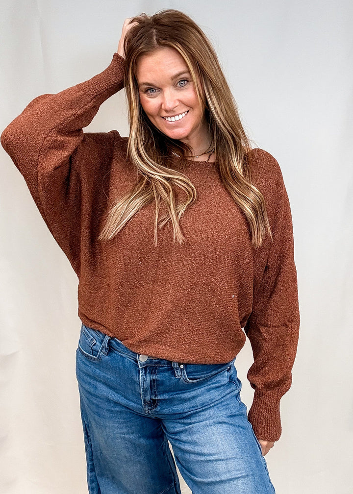 A woman wearing a brown fuzzy knit sweater and blue jeans, posing in front of a white studio backdrop.