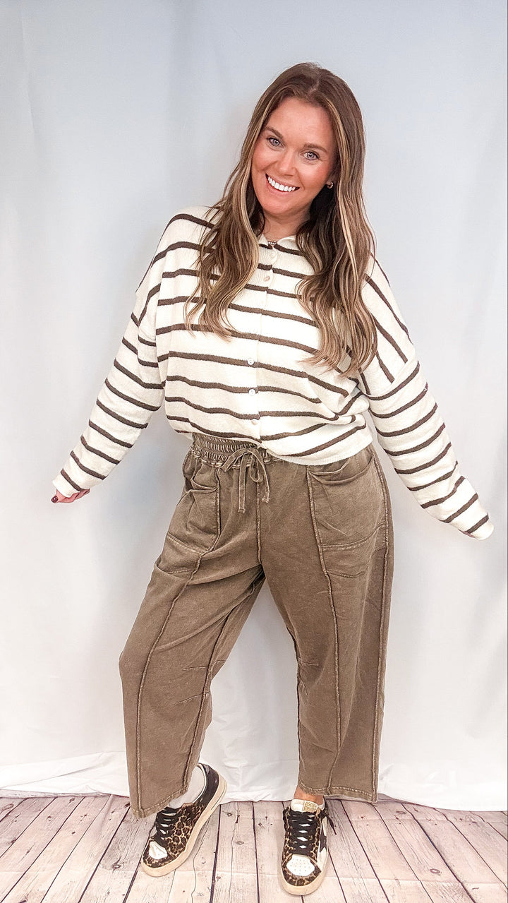 Woman wearing brown barrel sweatpants with white and brown stripe cardigan on white background