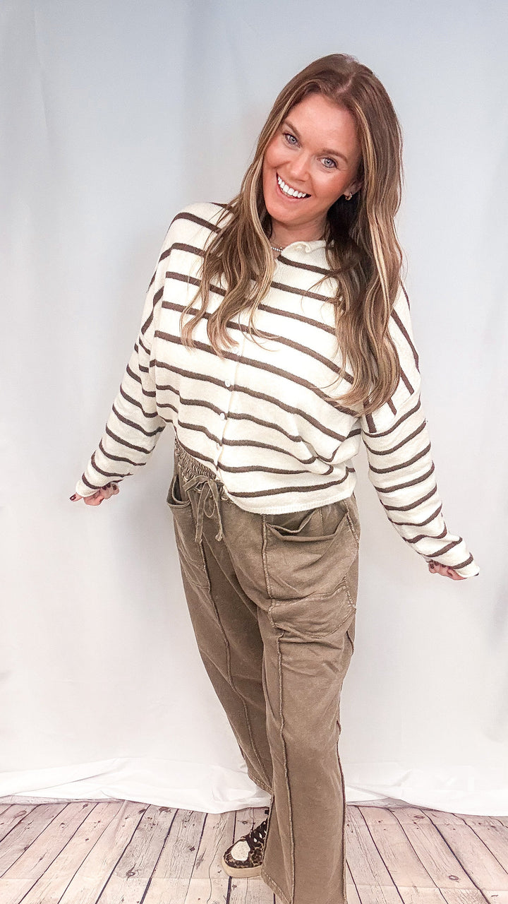 Woman wearing brown barrel sweatpants and white and brown stripe cardigan on white background