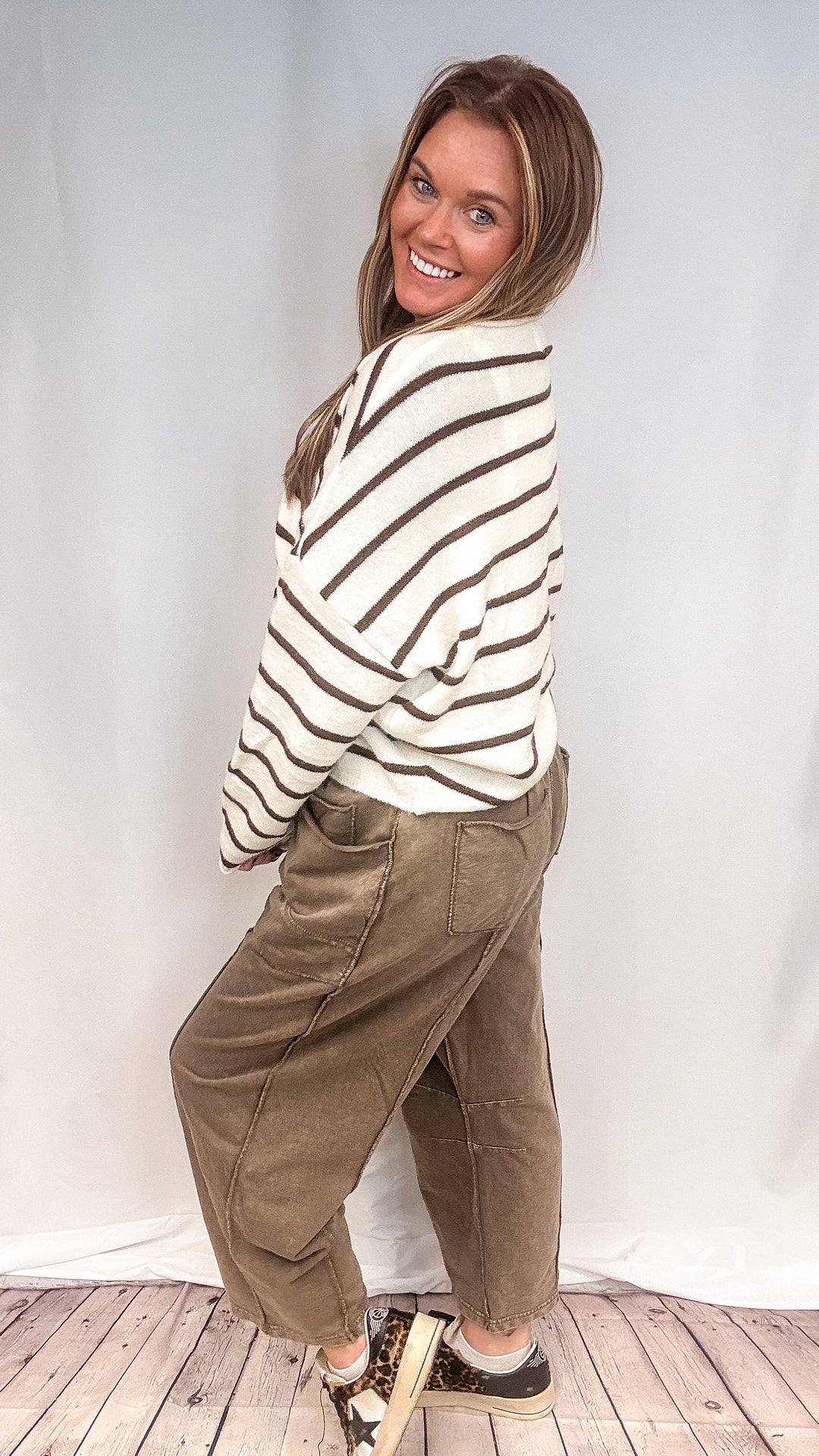 Woman wearing brown barrel sweatpants with brown and white stripe cardigan on white background