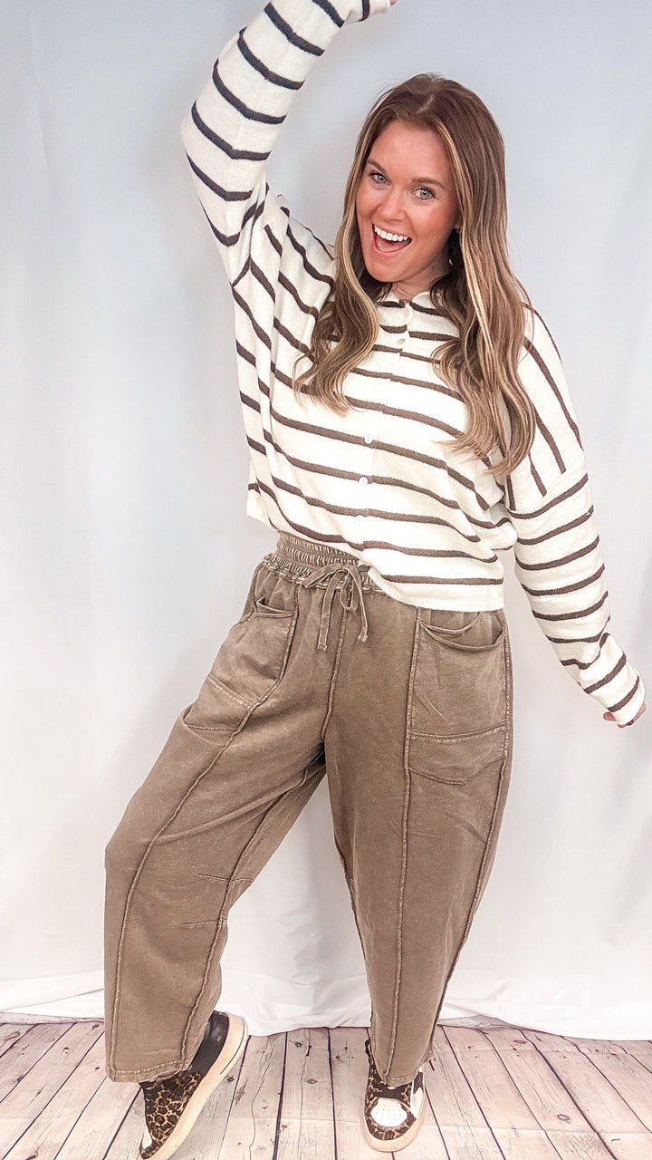 Woman wearing brown barrel sweatpants with brown and white stripe cardigan on white background