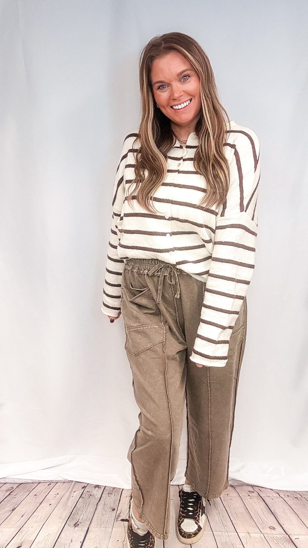 Woman wearing brown barrel sweatpants with brown and white stripe cardigan on white background
