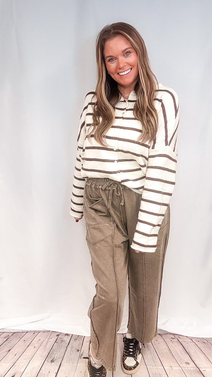 Woman wearing brown barrel sweatpants with brown and white stripe cardigan on white background