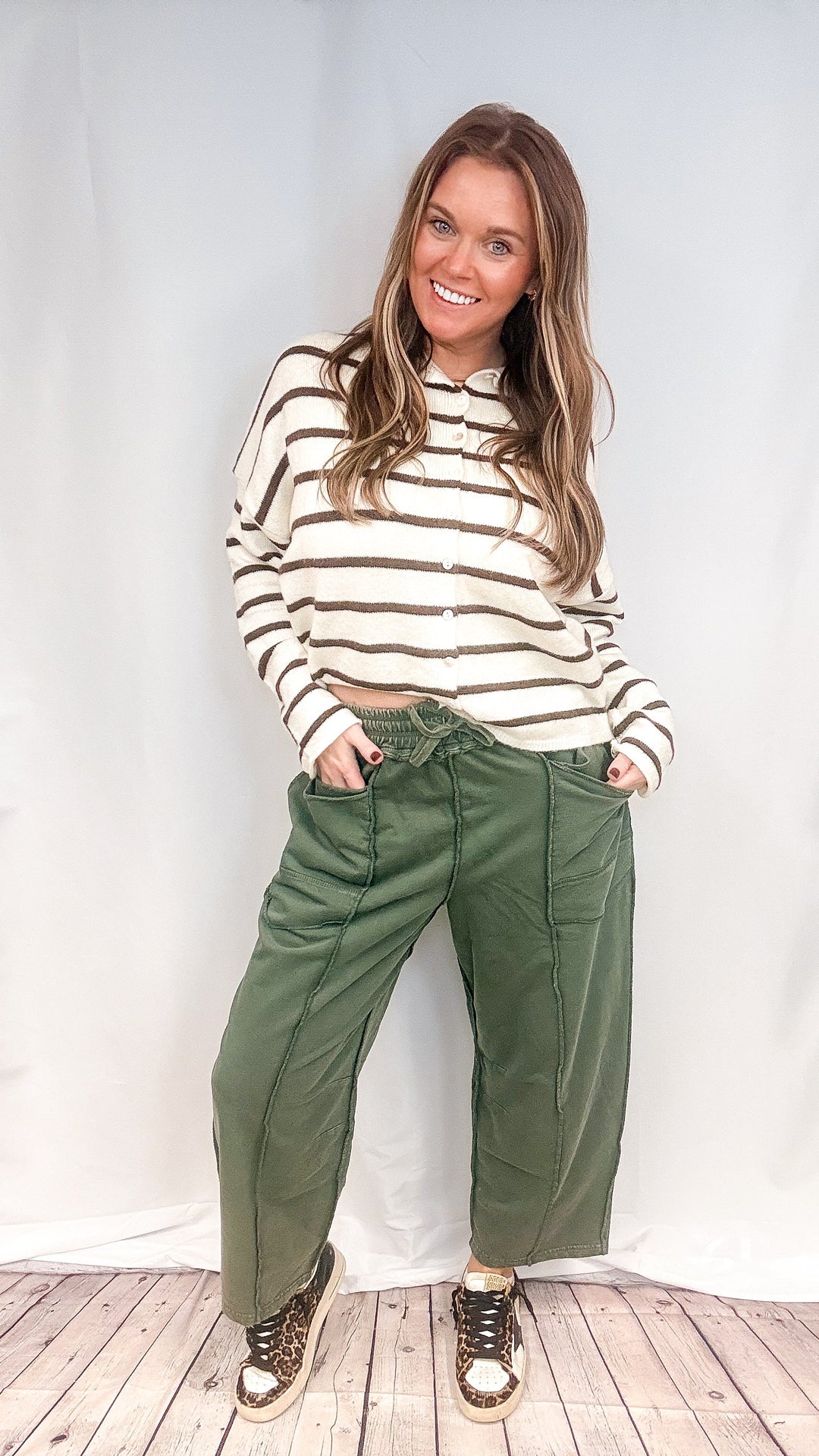 Woman wearing green barrel sweatpants and brown and white stripe cardigan on white background