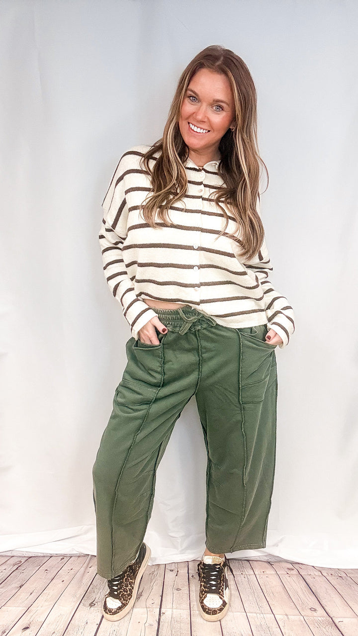 Woman wearing green barrel sweatpants and brown and white stripe cardigan on white background