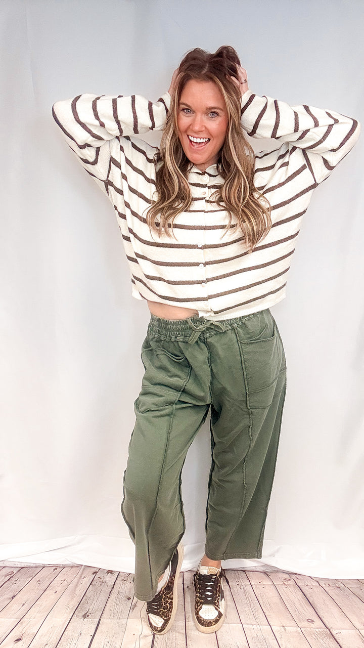 Woman wearing green barrel sweatpants with white and brown cardigan on white background