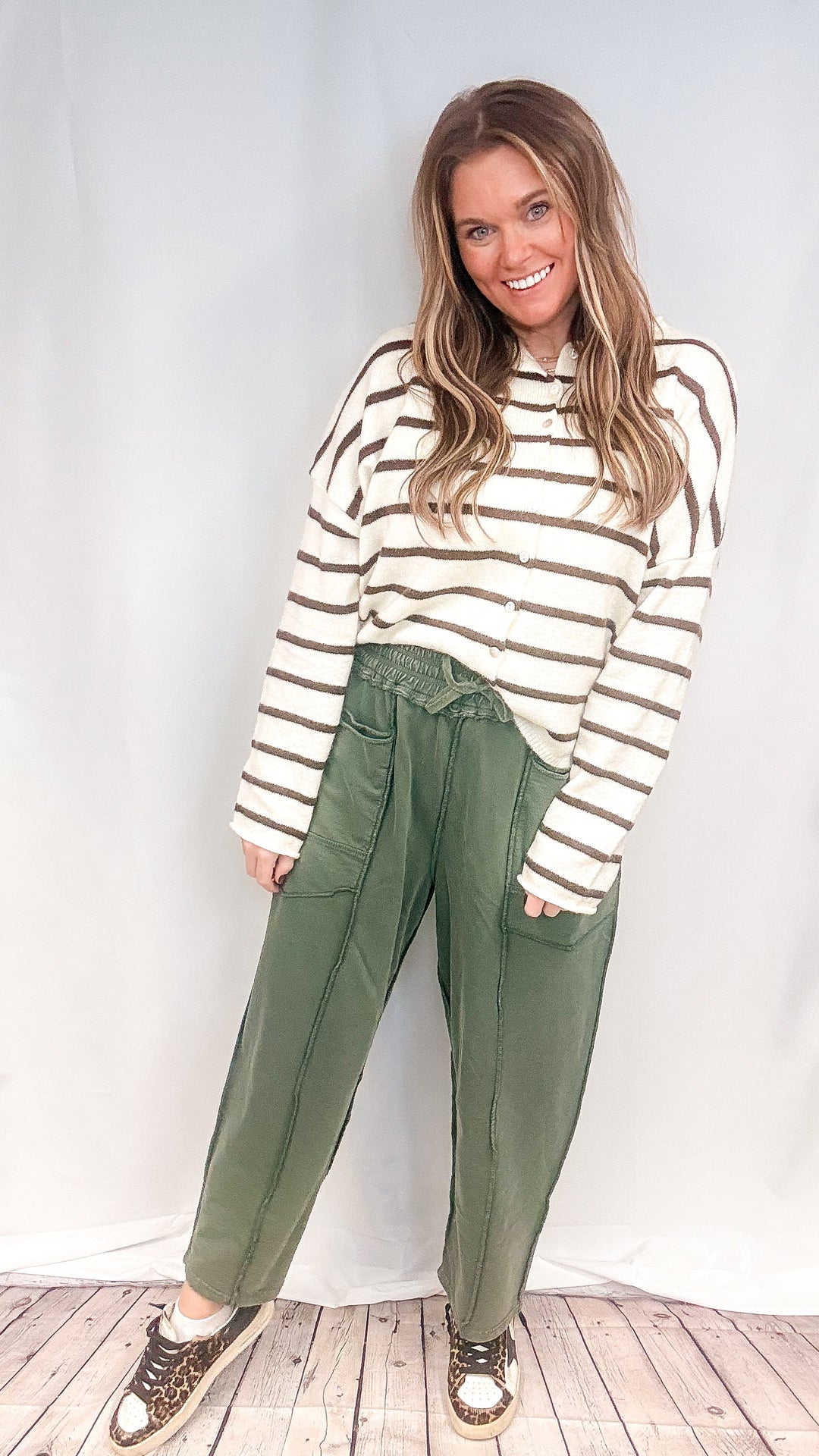 Woman wearing green barrel sweatpants with white and brown cardigan on white background