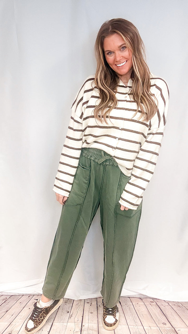 Woman wearing green barrel sweatpants with white and brown cardigan on white background