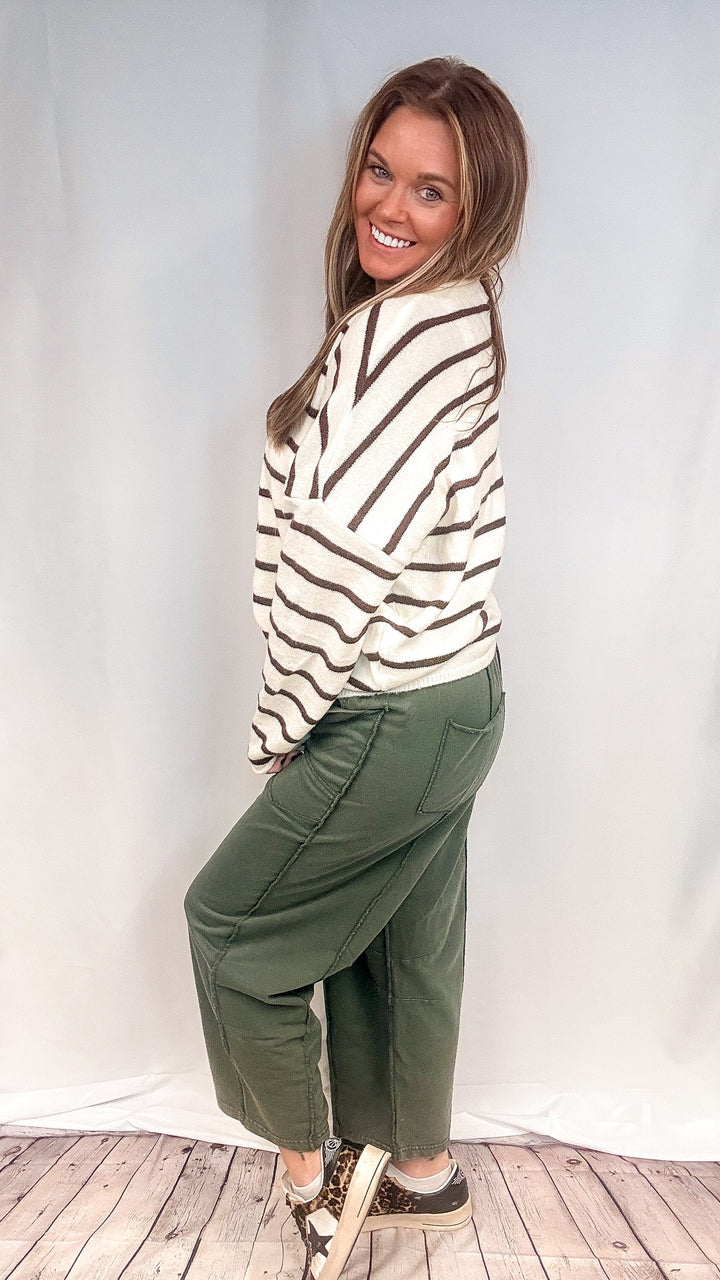 Woman wearing green barrel sweatpants with white and brown cardigan on white background