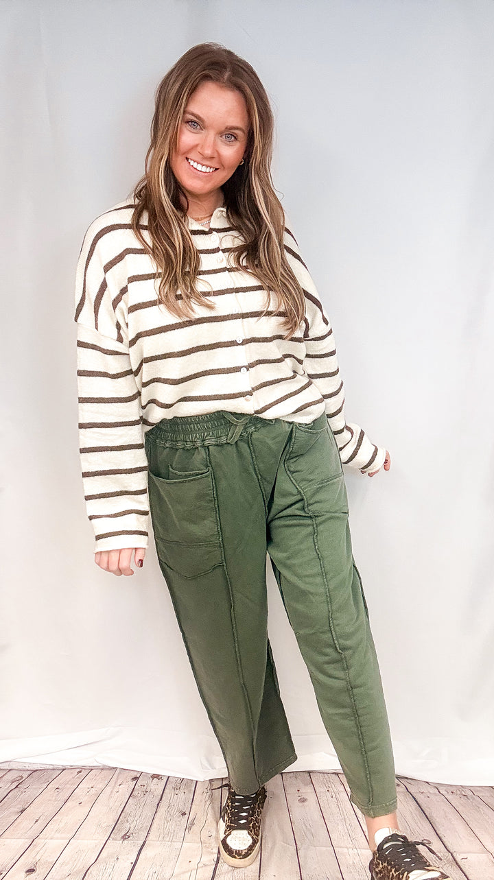 Woman wearing green barrel sweatpants with white and brown cardigan on white background