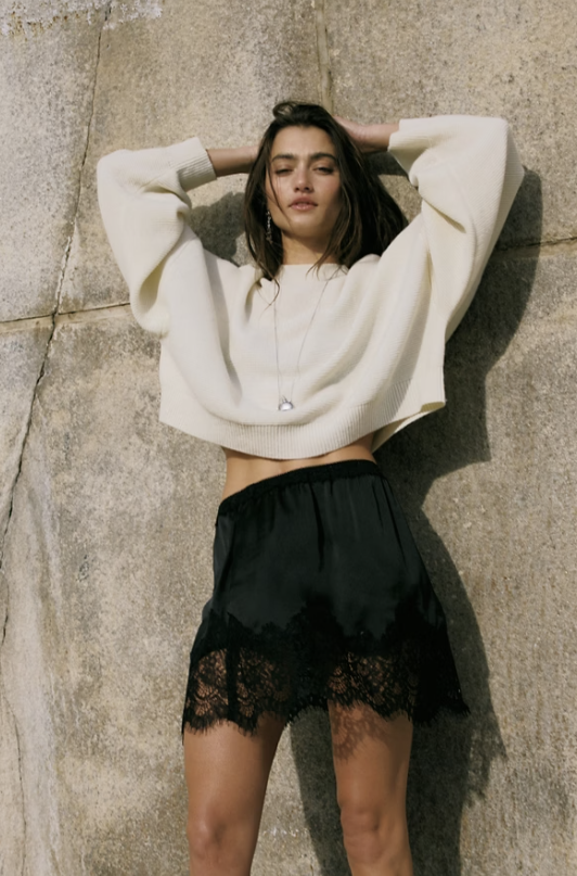 Woman wearing black slip skirt and white top on brick wall