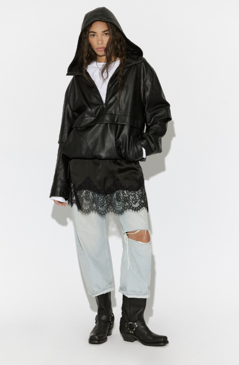Person wearing a black hooded jacket with lace details, light blue jeans, and black boots on a white background
