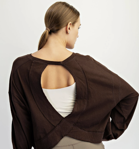 A woman shown from the back wearing a dark brown cropped long-sleeve top with a large keyhole cutout and crossover back detail, paired with taupe ribbed biker shorts against a light gray studio background.