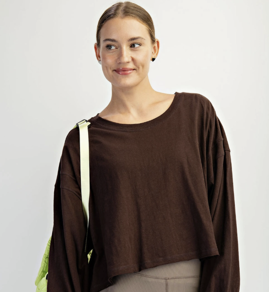 A woman modeling a dark brown long-sleeve cropped t-shirt and gray bike shorts, carrying a neon yellow-green shoulder bag against a light gray studio background.