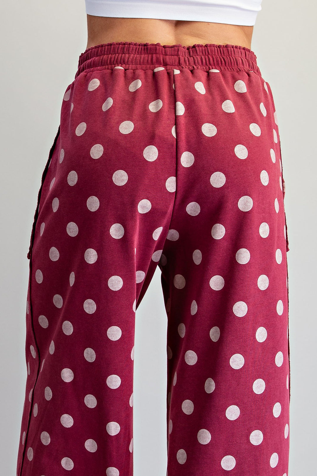 A close-up of a person wearing burgundy wide-leg sweatpants with a white polka dot pattern, shown from the back.