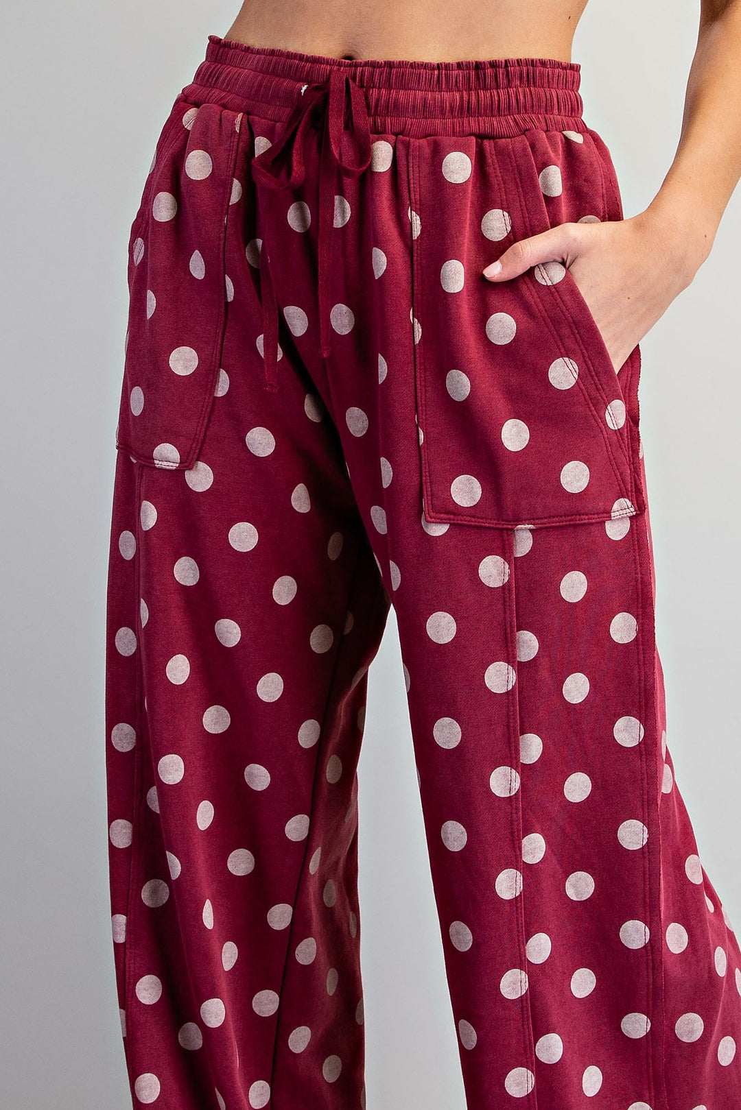 A close-up of a person wearing burgundy wide-leg pants with a white polka dot pattern, side pockets, and a drawstring waistband.