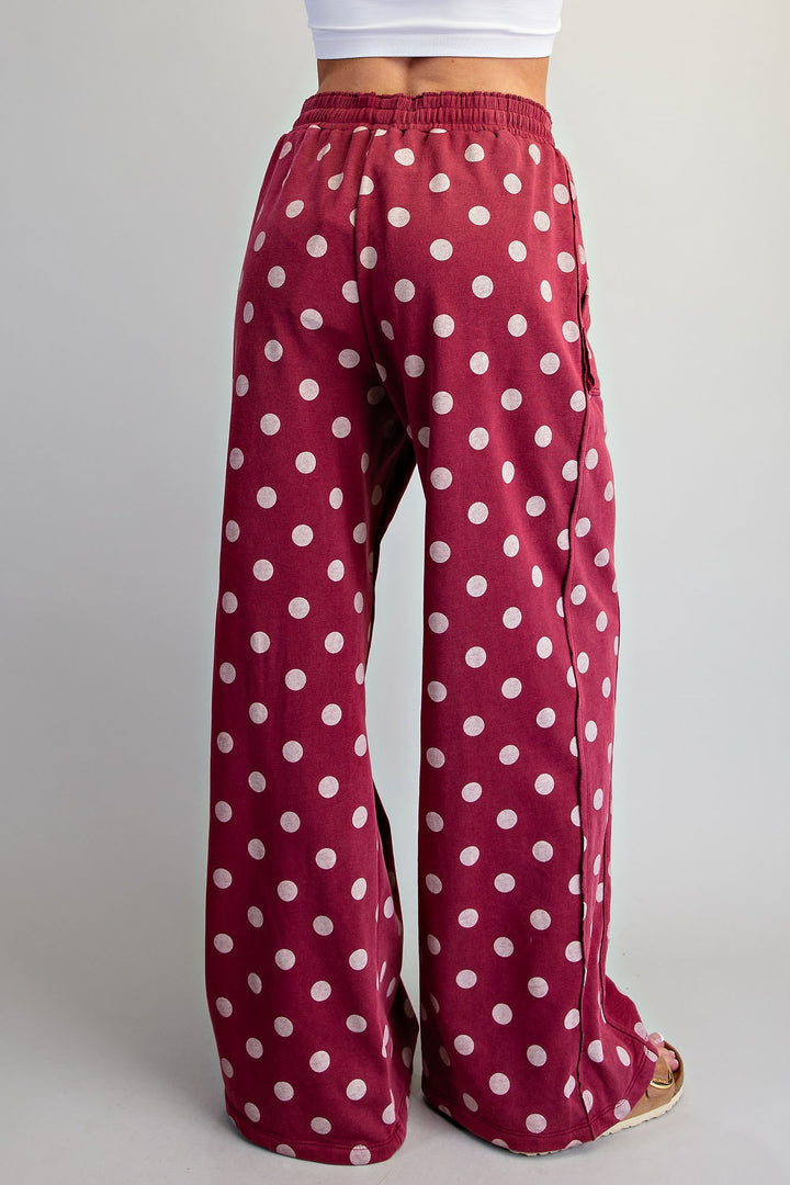 A person wearing wide-leg pants in burgundy with a white polka dot pattern, shown from the back against a light gray studio background.