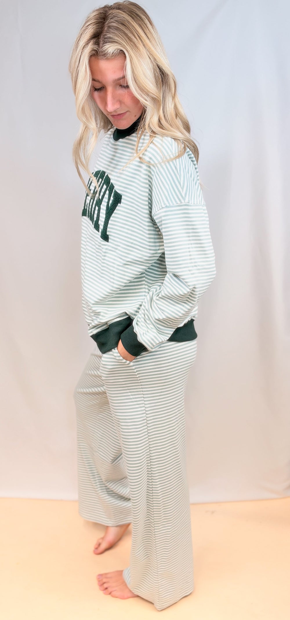 Woman shown from side view wearing matching sage and ivory stripe set on plain background