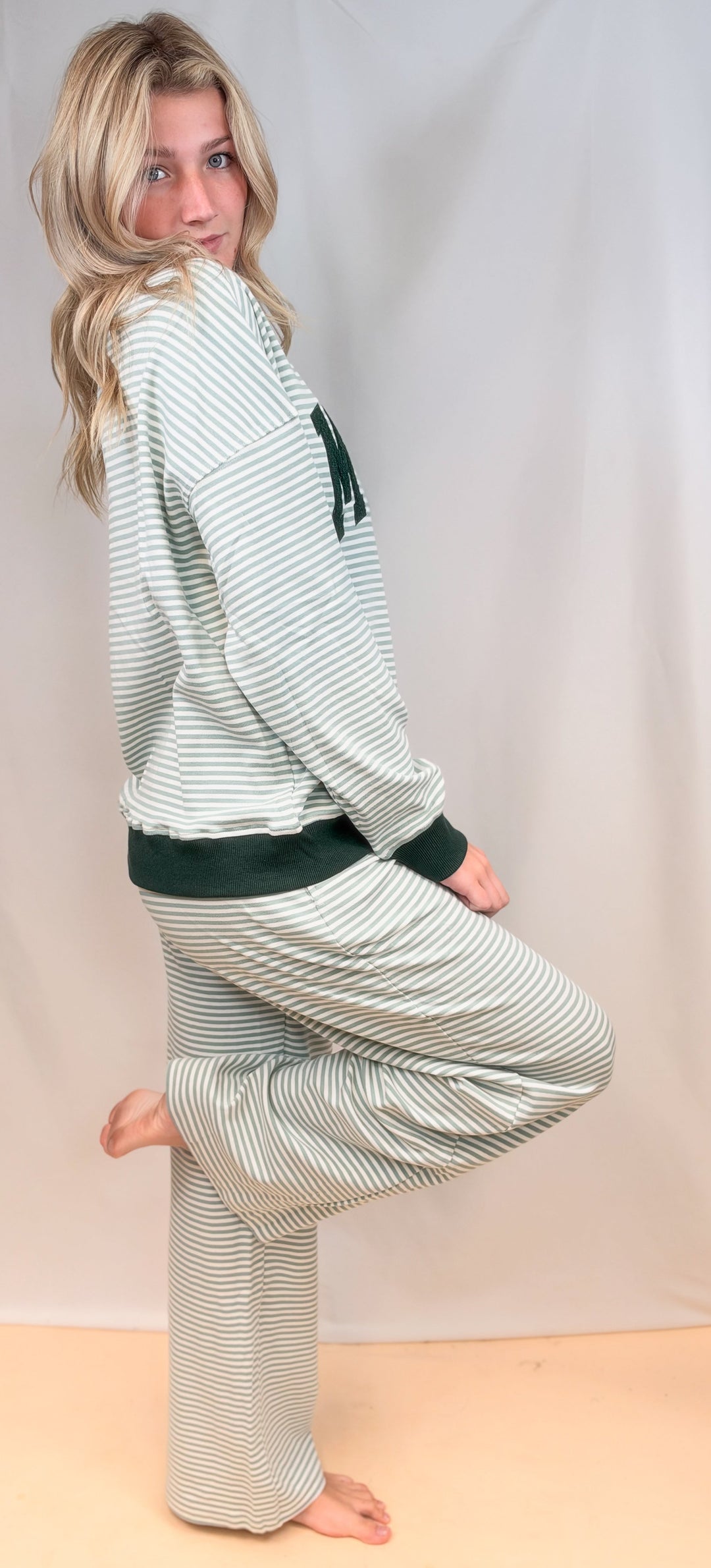 Woman shown from side view wearing matching sage and ivory stripe set on plain background