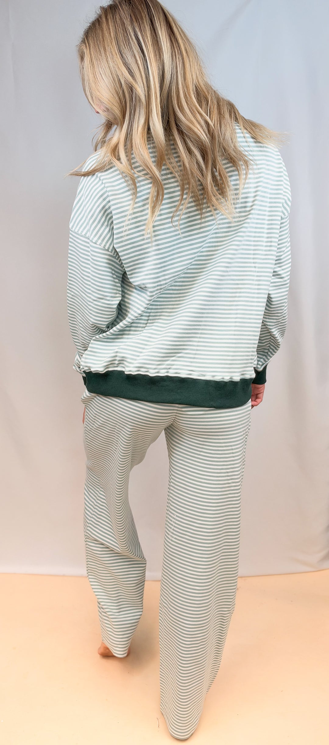 Woman shown from back wearing matching sage and ivory stripe set on plain background