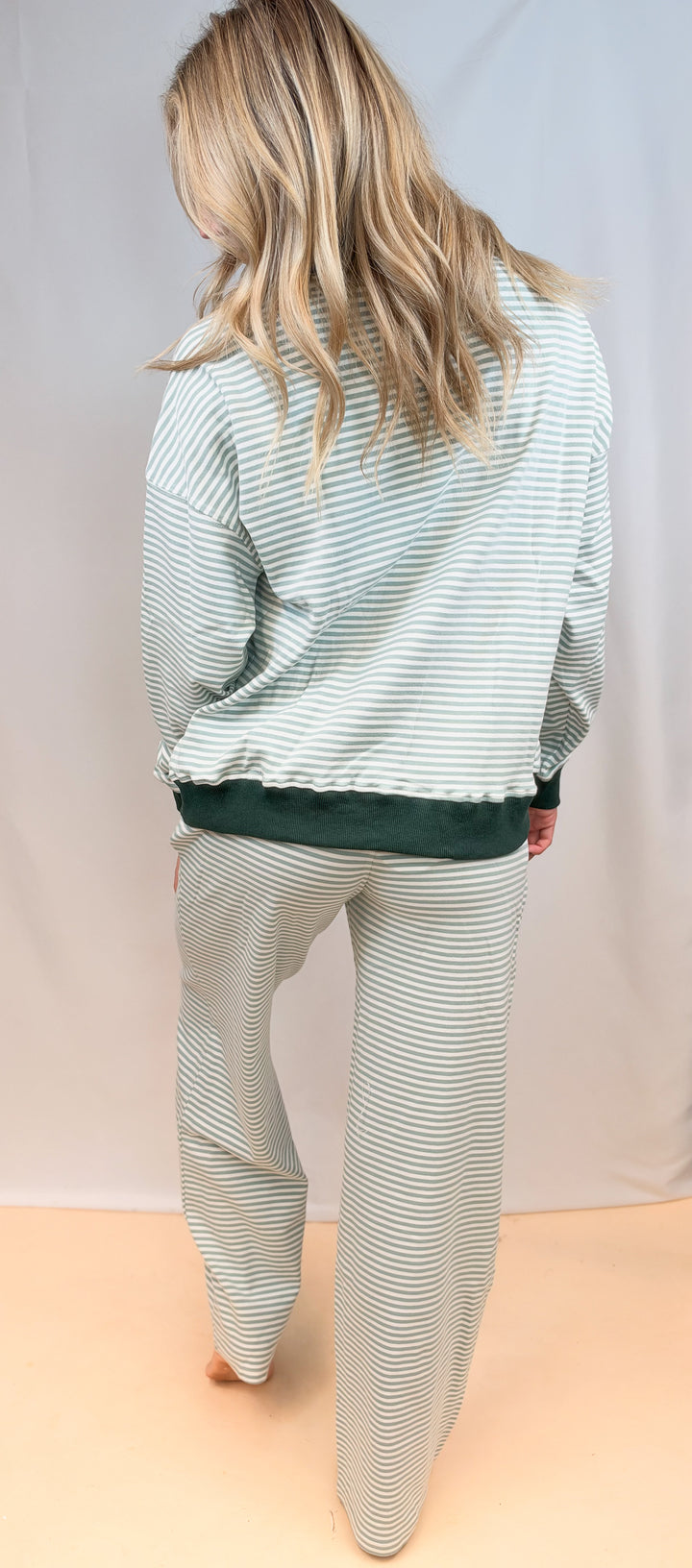 Woman shown from back wearing matching sage and ivory stripe set on plain background