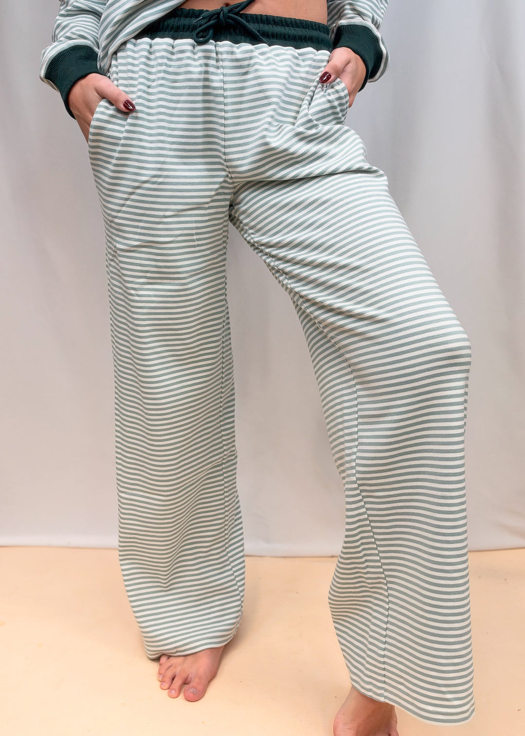 Woman shown from waist down wearing matching sage and ivory stripe set on plain background