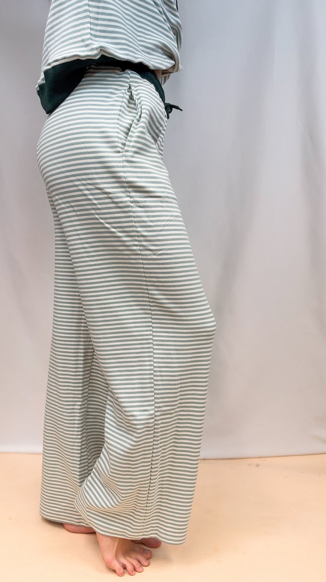 Woman shown from side view, waist down wearing sage and ivory stripe set on plain background