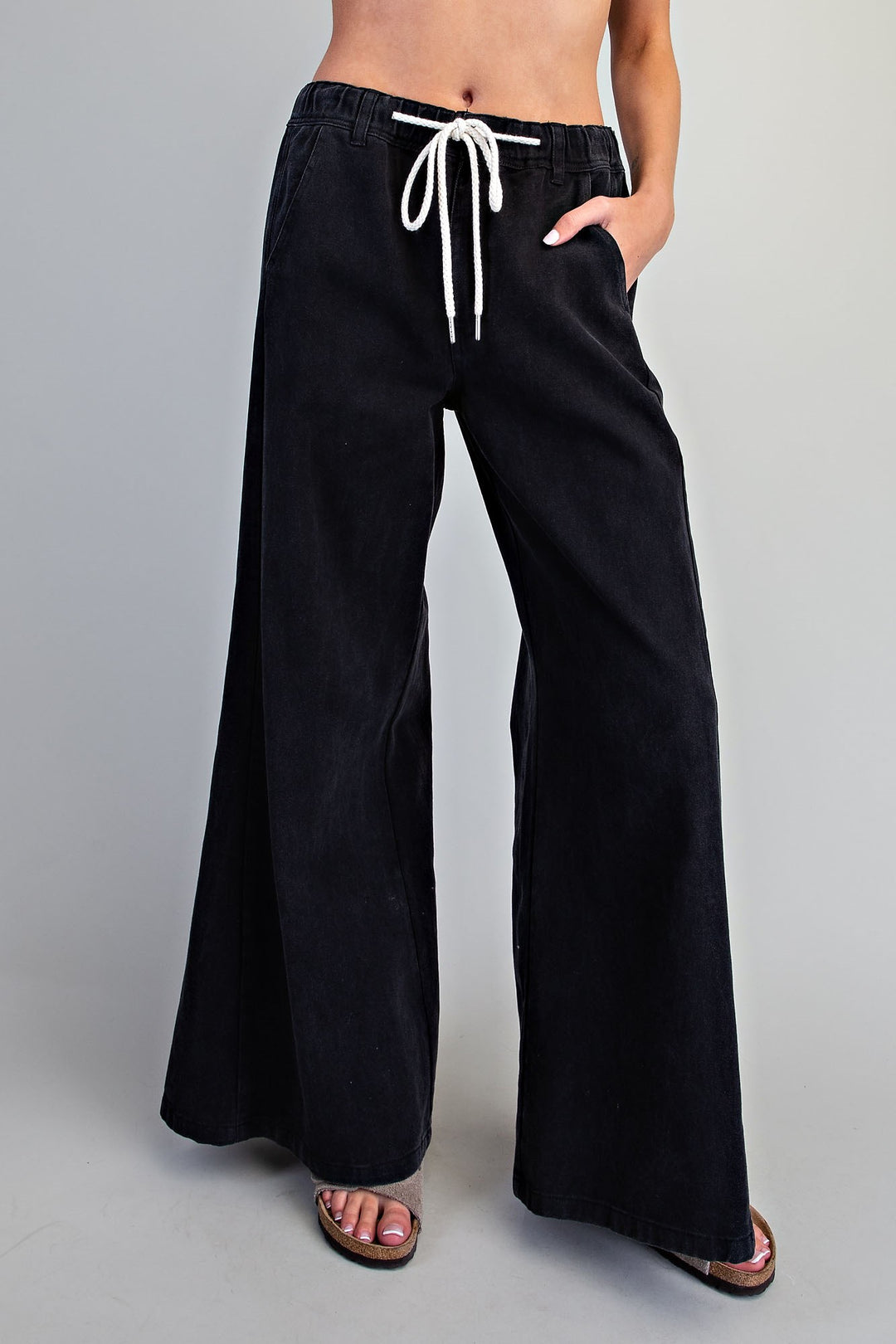 Black wide-leg pants with a white drawstring, shown on a model from the waist down against a light gray studio background.